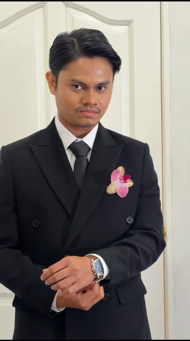 A man in a black suit adjusting his cuff beside a white door