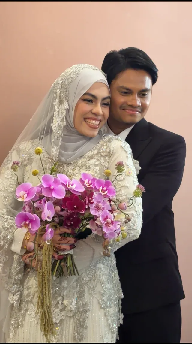 A smiling couple posing together with a bouquet of purple orchids